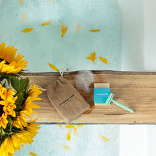 Load image into Gallery viewer, Mint green safety razor with natural shaving soap and drawstring hessian bag, on a log tray over a bath, with sunflowers at the forefront - Shoreline Shaving
