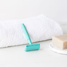 Load image into Gallery viewer, Teal safety razor resting on a white towel with the logo on the head plate in view, next to a shaving soap bar - Shoreline Shaving
