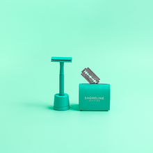 Load image into Gallery viewer, Razor blade disposal tin next to a reusable safety razor and stand - Shoreline Shaving