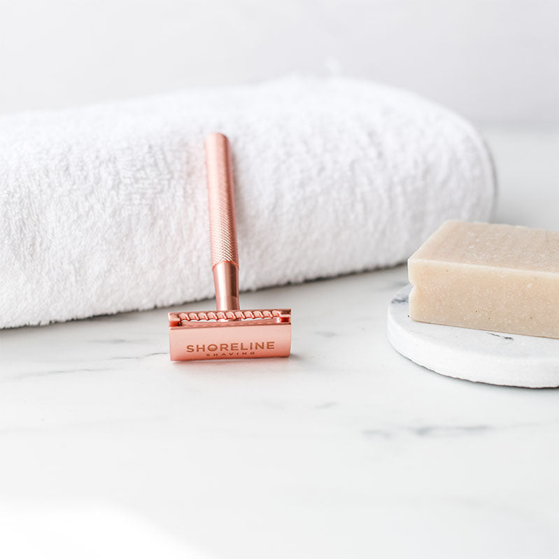 Closeup of rose gold single-blade safety razor leaning on a white towel - Shoreline Shaving