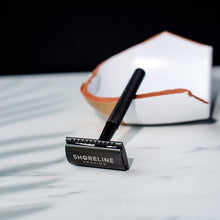 Load image into Gallery viewer, Closeup of matte black safety razor with the Shoreline Shaving logo in view
