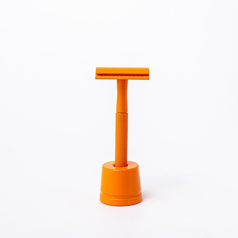 Vivid orange reusable metal safety razor inside an orange razor stand - Shoreline Shaving