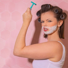 Load image into Gallery viewer, A woman holding a metal teal safety razor aloft, while having rollers in her hair and shaving foam on her face - Shoreline Shaving
